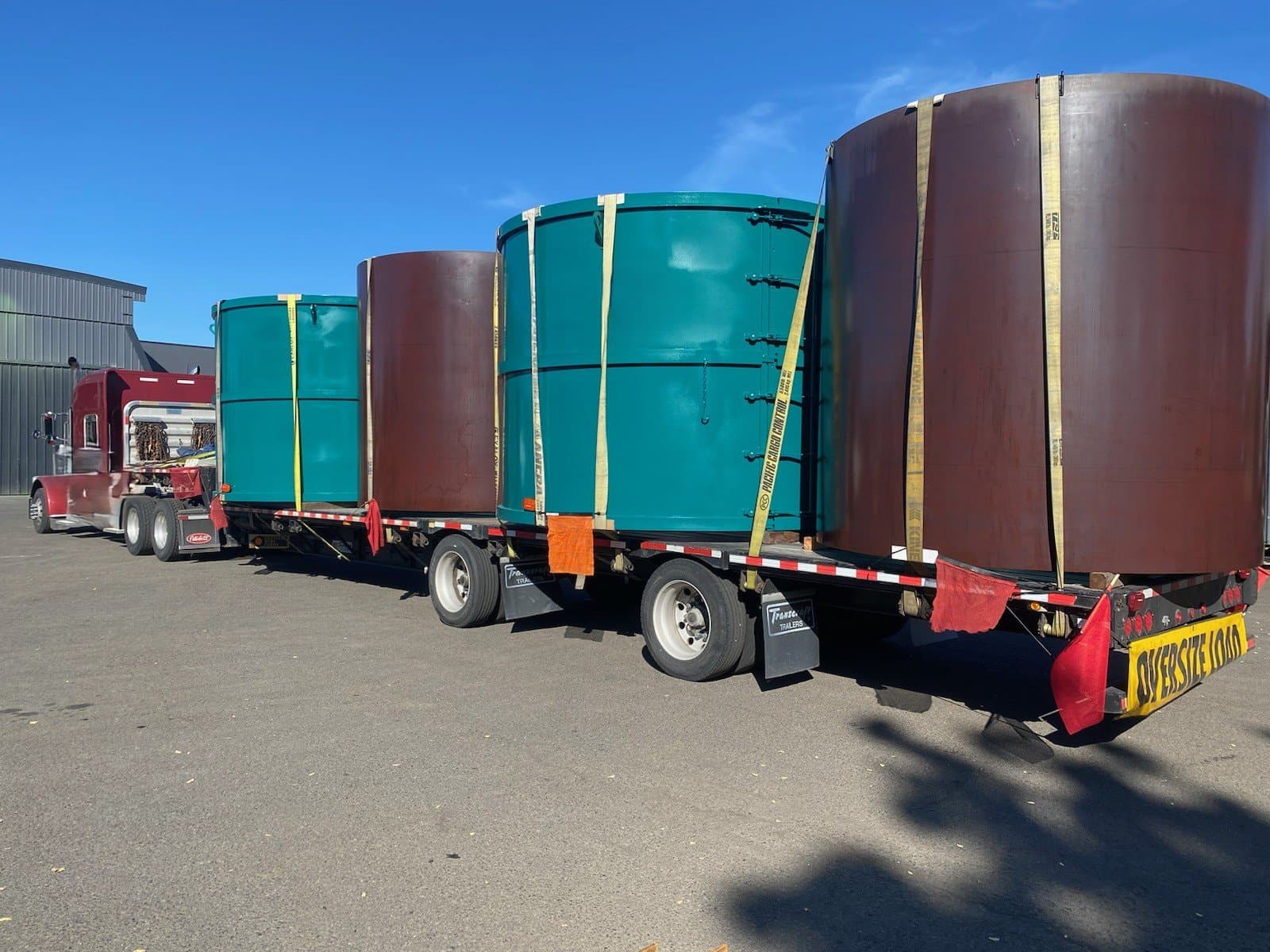 Oversized cylindrical steel tank forms on step deck trailer
